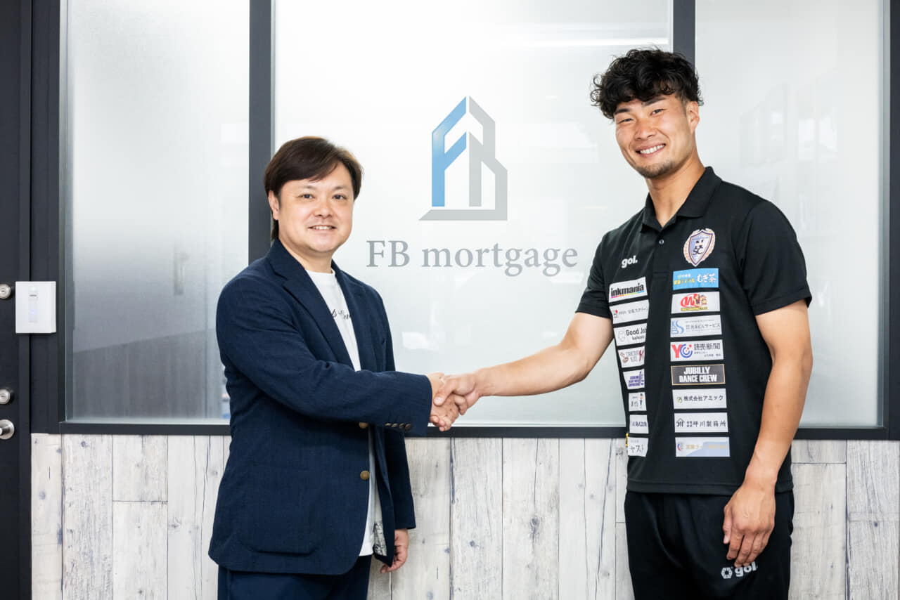 南葛SCの営業担当の外山佳大さんと根石社長が握手している写真